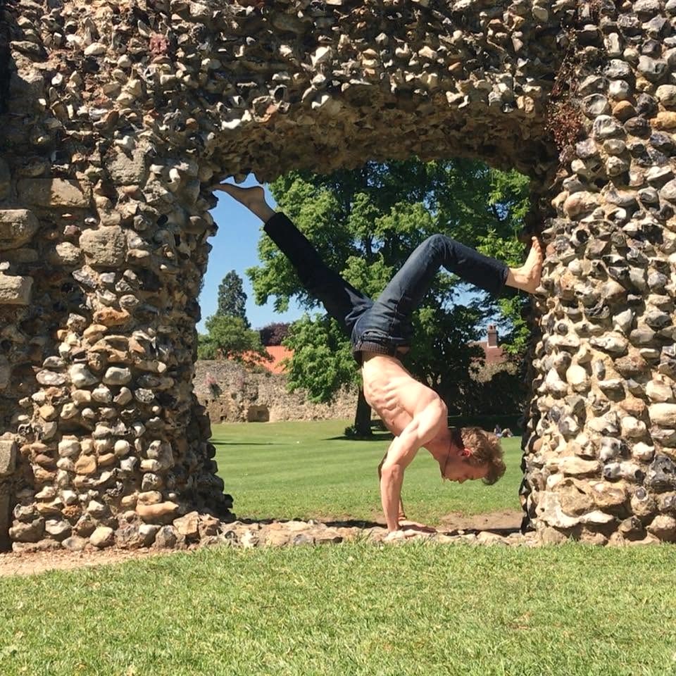 David in a shirtless press-handstand framed by a ruined flint arch