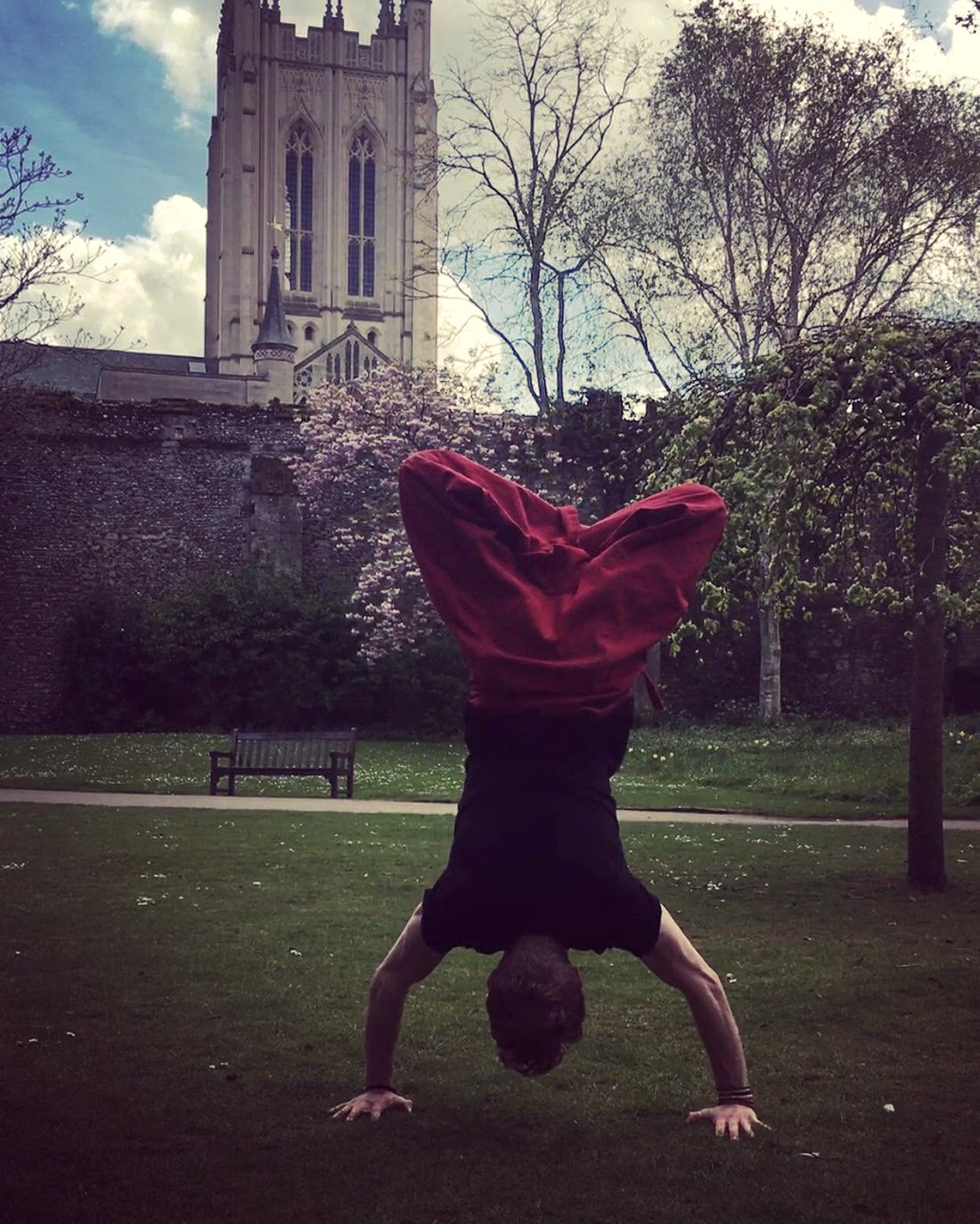 David in a handstand on the grass below a cathedral tower